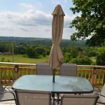 The deck has a table with sun umbrella, chairs and a BBQ